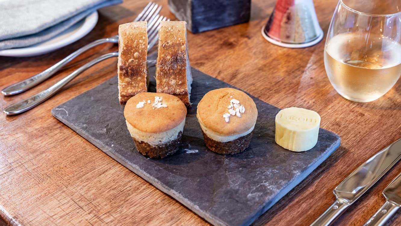 Bread and cakes on a slate plate on a table with cutlery and a wine glass in view