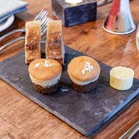 Bread and cakes on a slate plate on a table with cutlery and a wine glass in view