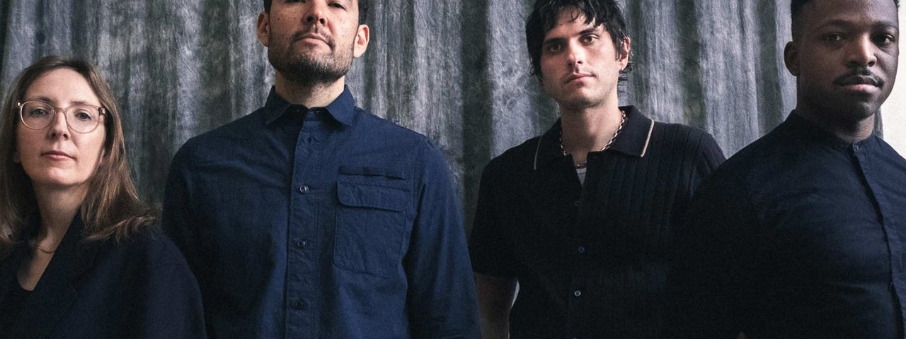 4 serious looking people in a line, dressed in dark clothes.