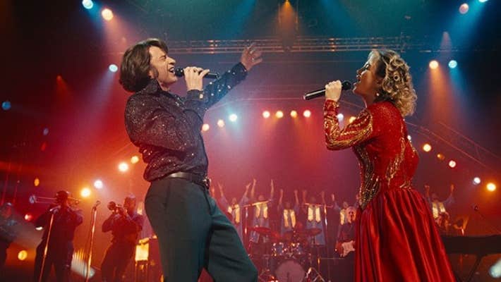A man and woman singing with passion into mics, facing each other on a stage.