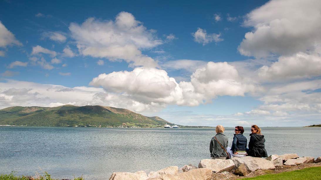 Three people looking at a mountain on the far side of a lake in Carlingford County Louth