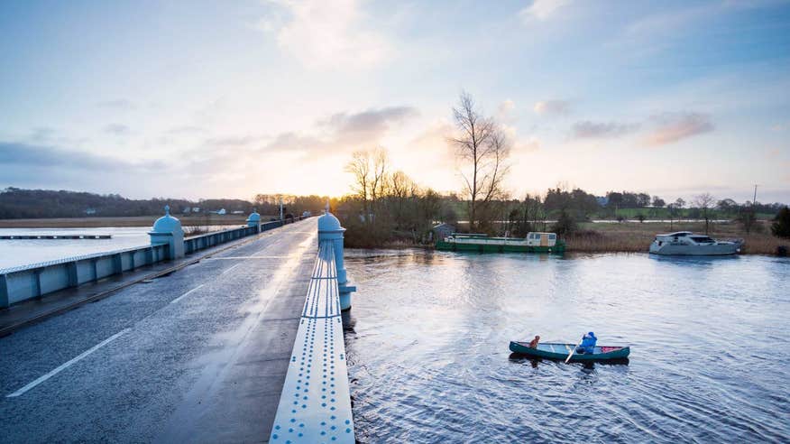 Woman paddling a canoe under Portumna Bridge in Galway with a dog sitting at the front