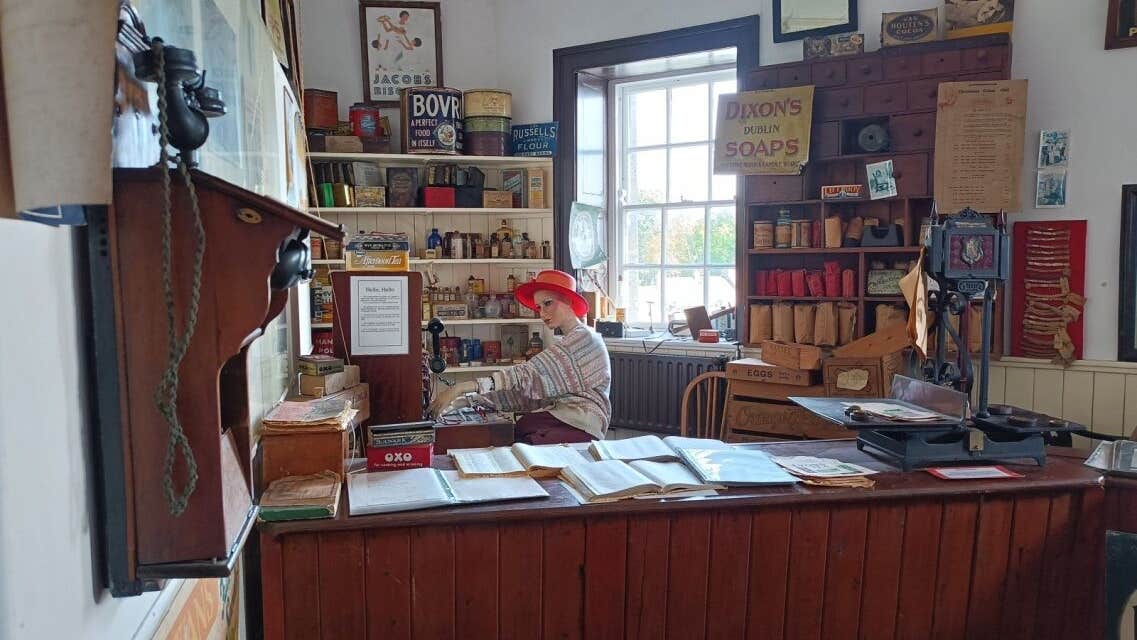 Exhibition with a mannequin behind a desk with books and posters and shelves in the background