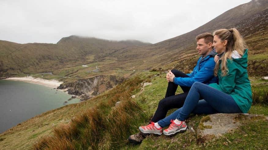 A man and woman wearing jackets looking out to Keem Bay from a hill