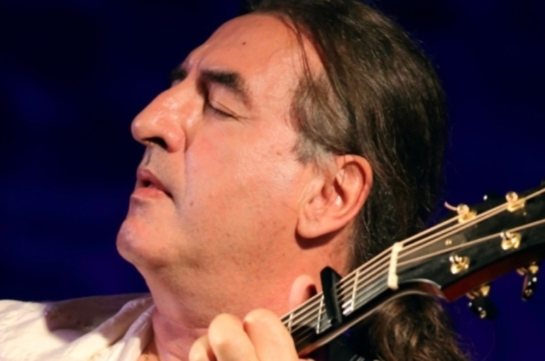 Close up headshot of man with eyes close and his left hand on the neck of a guitar.