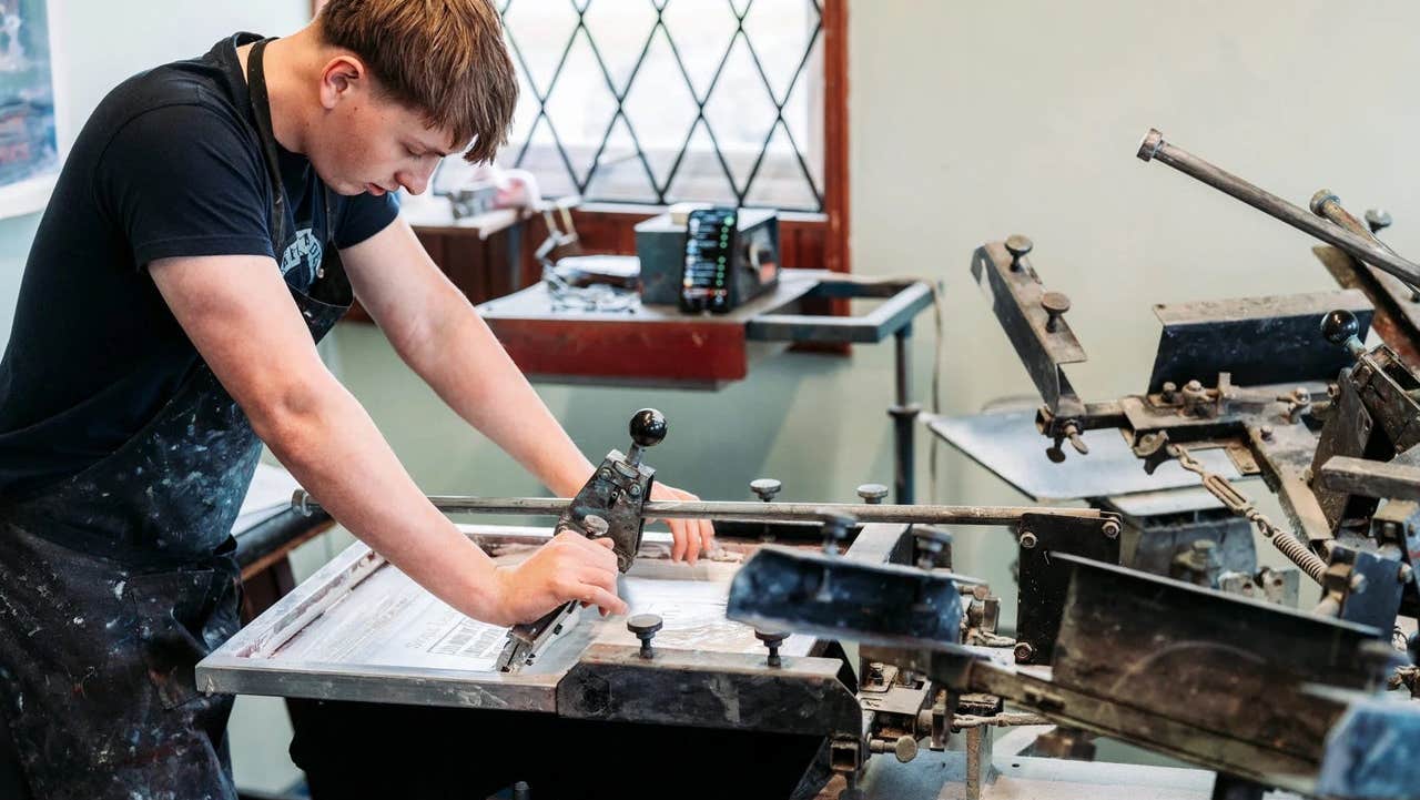 A person working at a screen printing station using a large manual press in a workshop