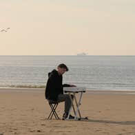 James Malikey - Lost Within The Aether, a man seated at a small portable keyboard on an empty beach