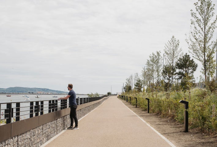 A man looks out towards the boats at sea in Dublin bay from the Greenway path