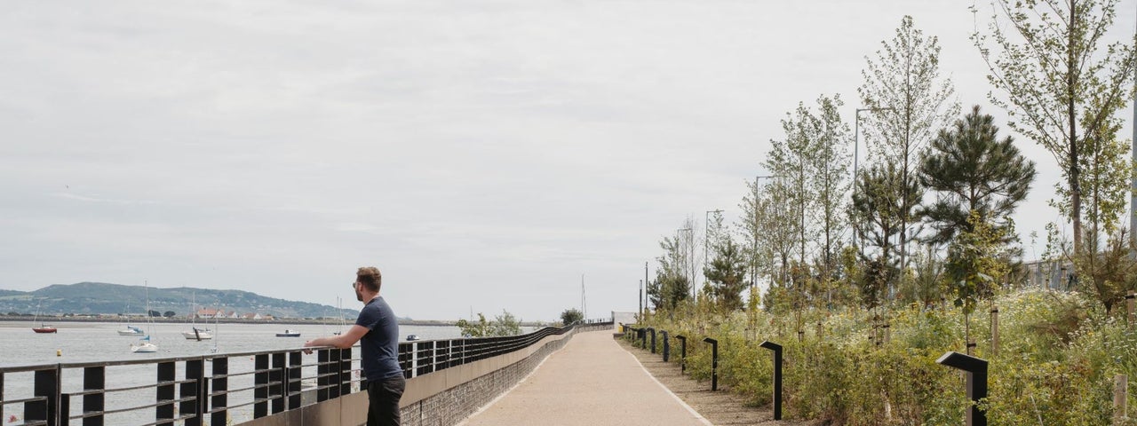A man looks out towards the boats at sea in Dublin bay from the Greenway path