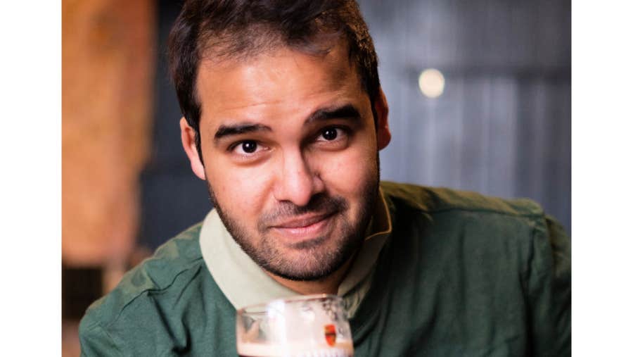 A gently smiling man holding up a pint of stout
