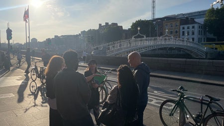 A group gathered beside a bridge on a sunny day taking part in a walking tour along the River Liffey