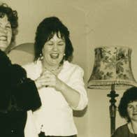 Old photo of 2 women standing and laughing with seated woman holding pipes.
