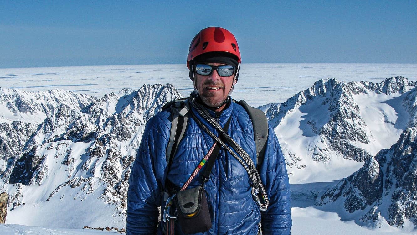 A man in mountaineering gear including helmet and sunglasses on snowy mountain