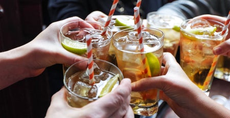 A close up of several hands holding whiskey glasses in a toast