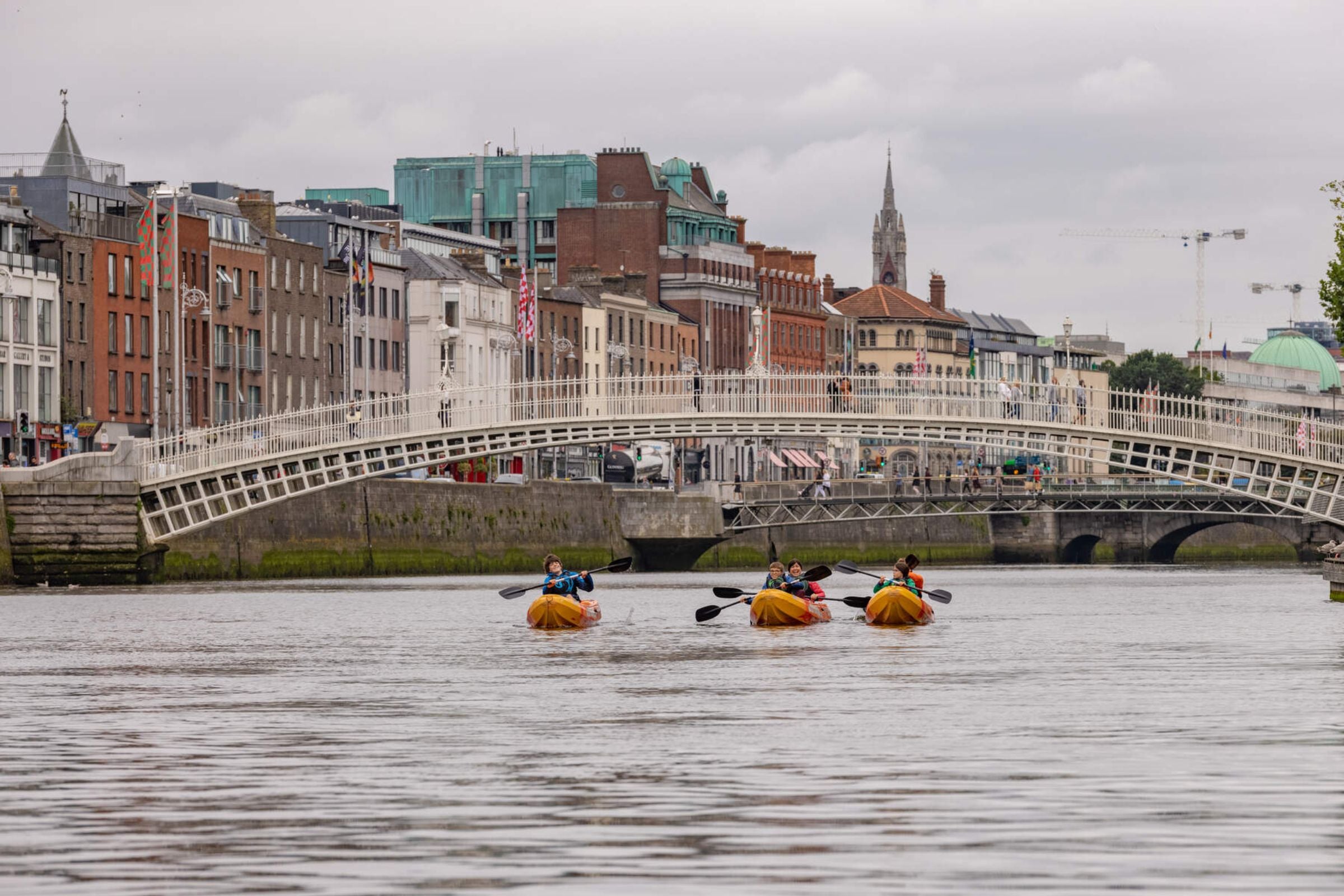 Four kayakers going under Ha'Penny Bridge on the River Liffey in Dublin City.