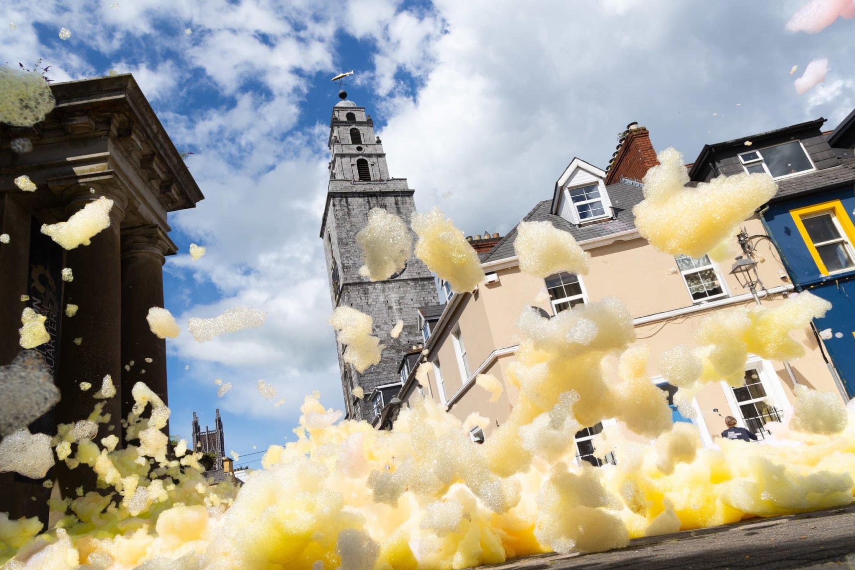Cork Midsummer Festival (photo by Jed Niezgoda) A view of a street looking up from the ground, buildings partially obscured by large clumps of yellow foam.