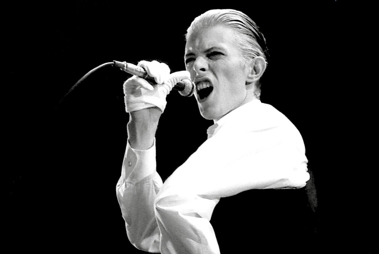 Black and white photo of Bowie singing into a microphone