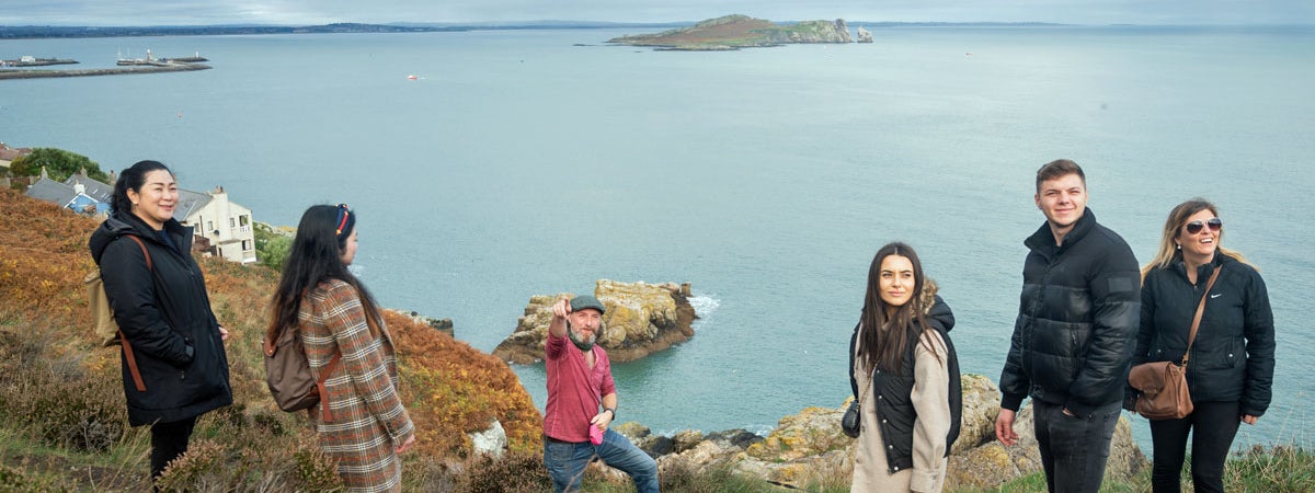 A guide with a group on Howth Cliffs with the sea in the background