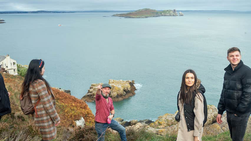 A guide with a group on Howth Cliffs with the sea in the background