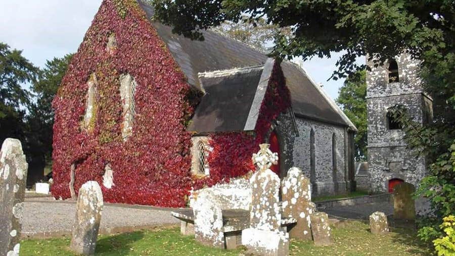 View of the ivy covered gable of the church with headstones visible in the forefront