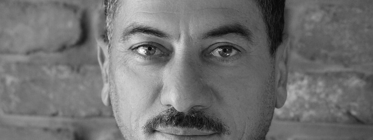 Black and white headshot of man with moustache with slight smile.