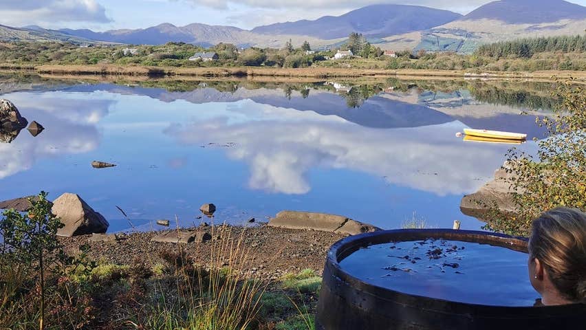 A woman relaxes in a seaweed bath looking out over a lake