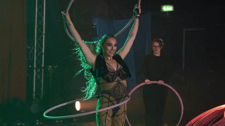 A smiling woman in circus ring holding up hoola hoop