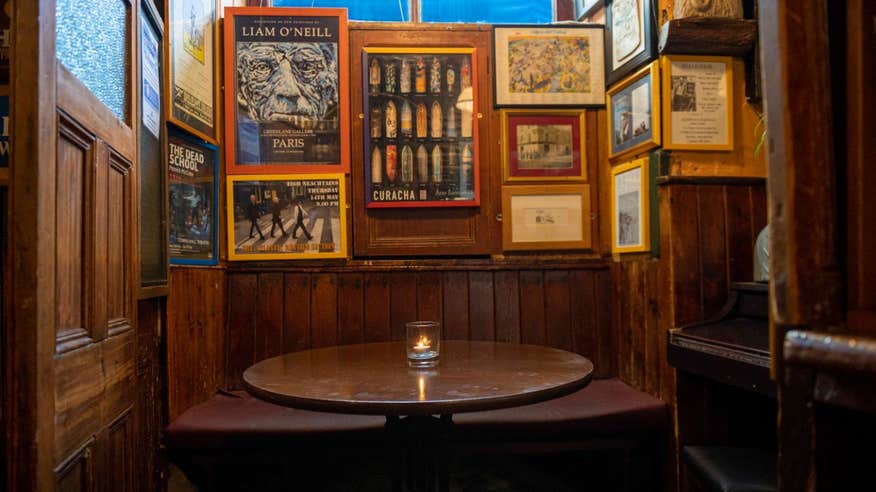 A snug in a traditional Irish pub with wooden walls. On the wooden table is a single candle and posters frame every inch of the walls.
