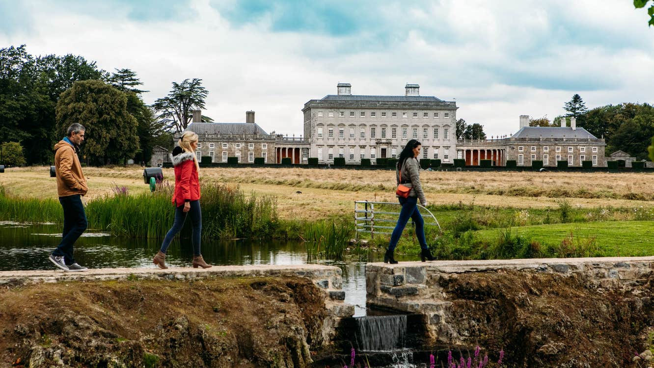Three people walking on a path in front of Castletown House, Co Kildare