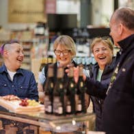 Four people standing at a counter with wine and food on it