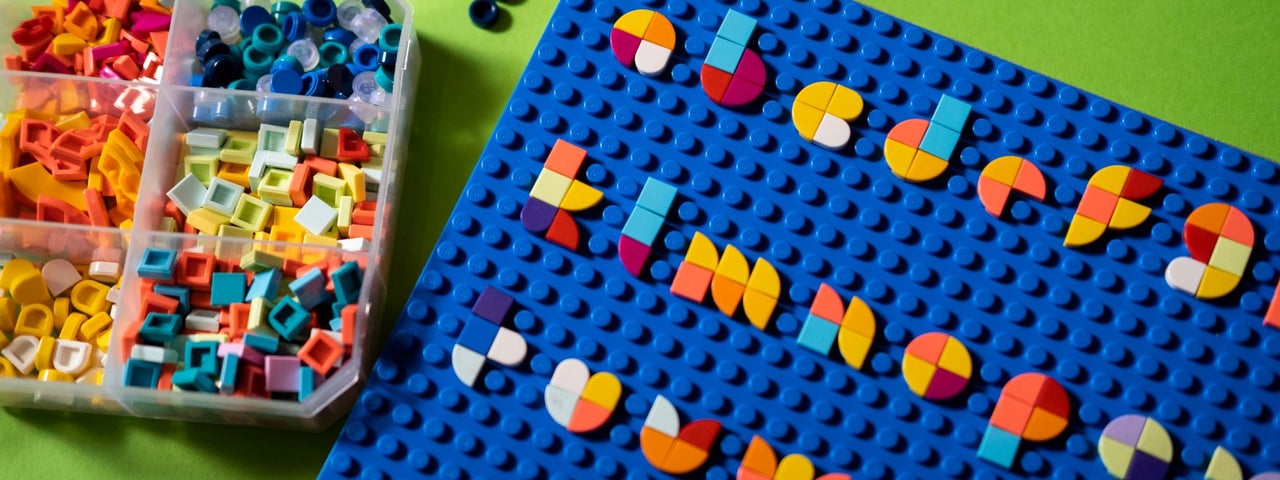 The alphabet made in multi coloured LEGO on a blue board with a box of pieces next to it.