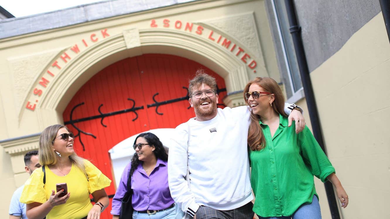 Group of people smiling leaving a building with red arched doors