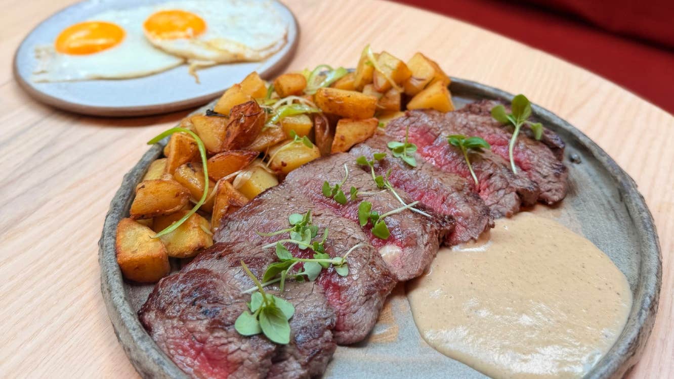 A plated steak dish with roasted potatoes and a creamy sauce with two fried eggs on a side plate