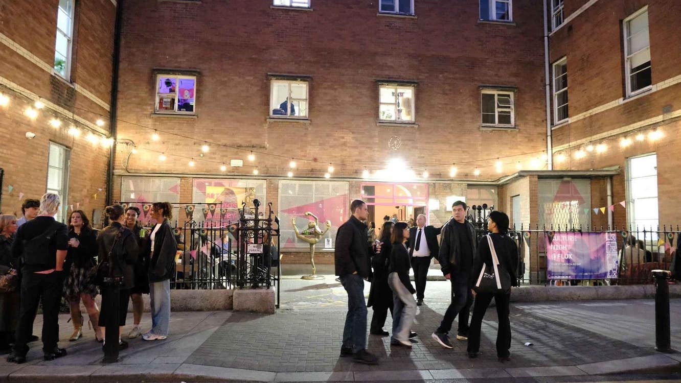 Exterior of a building at night with a courtyard and people and lights