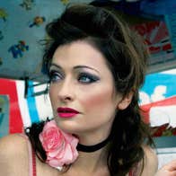 A woman with dark make-up is holding an ice cream looking away to her right.