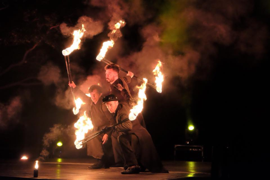 ROGU - Fire Show and Movement Arts. At night, 3 men in dark gowns holding sticks with the ends on fire.
