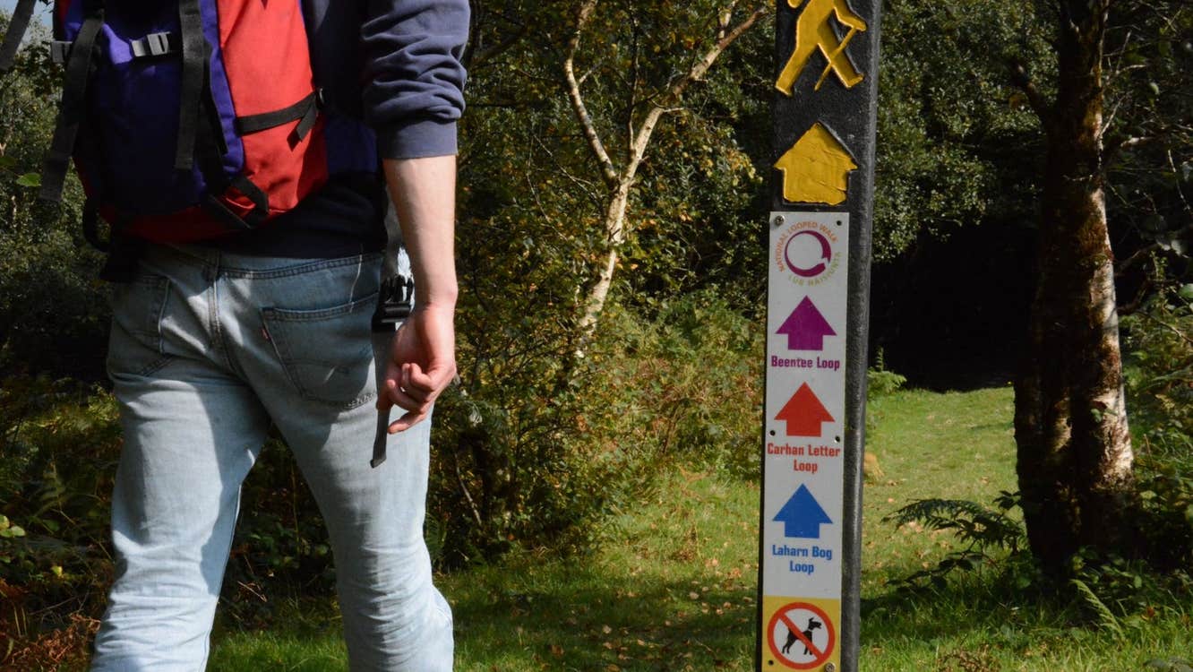 A person with a backpack walking on a path with a trail marker sign