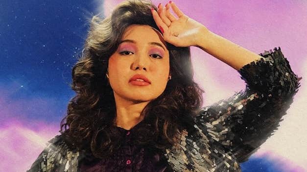 A woman is holding up the back of her hand to her forehead in a slightly dramatic manner.