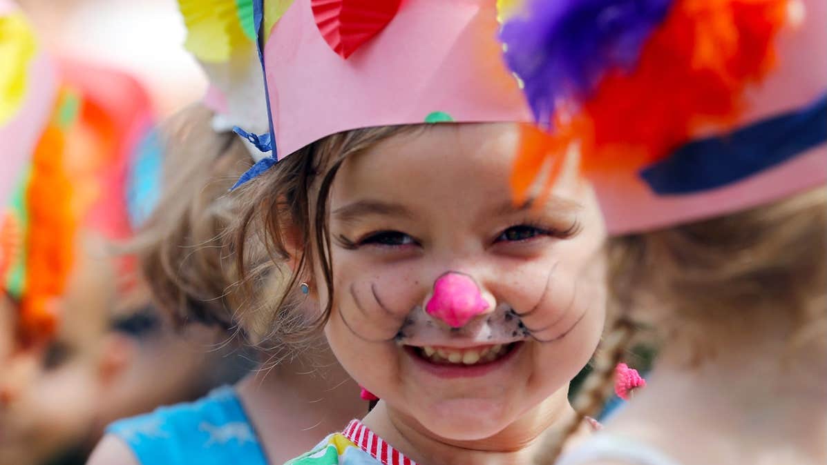 A very young smiling girl wearing a hand made pink crown and face painted.
