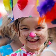 A very young smiling girl wearing a hand made pink crown and face painted.