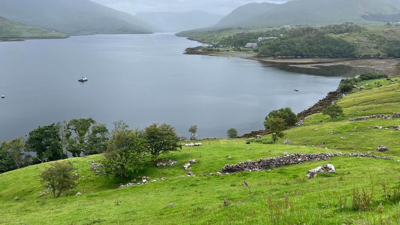 Lush green hills overlooking a calm lake surrounded by misty mountains