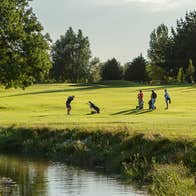 Golfers playing a round of golf on the green at Dungarvan Golf Club with trees and a pond