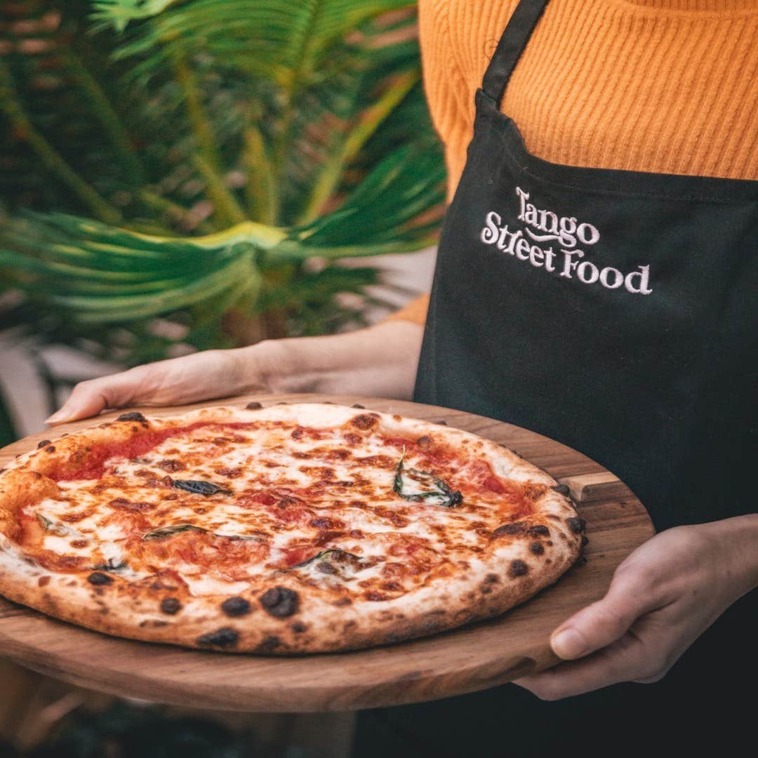 A person holding a pizza on a wooden plater from Tango Street Food in County Kerry.