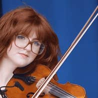 A serious looking young woman holding a violin and bow ready to play
