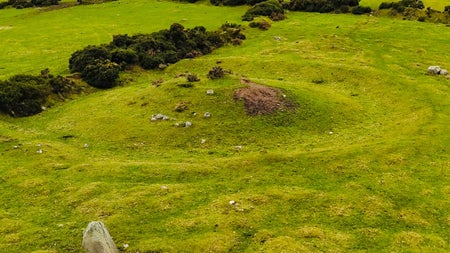 A drone shot of that shows a granite standing stone in the foreground with a burial mound called a barrow behind it in the centre of the image