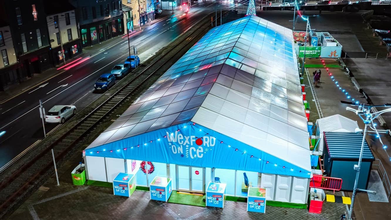 A large tent by a road in a town, lit up a night in white and blue