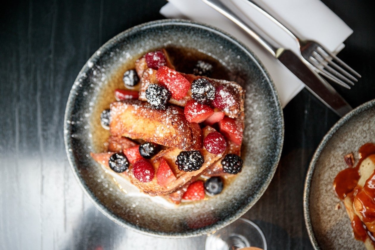 French toast decorated with berries, maple syrup and icing sugar.