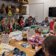 A group of people seated around a large table covered in craft items, working and talking.