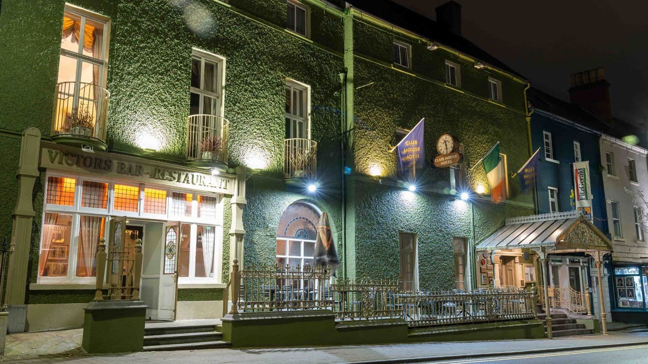 Exterior of a restaurant covered in ivy with flags on display and railings in front