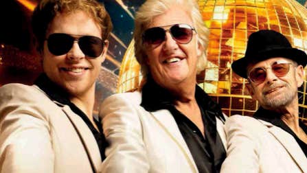 3 smiling men in white suits with dark shirts, all wearing sunglasses with golden, mosaic disco ball in background.